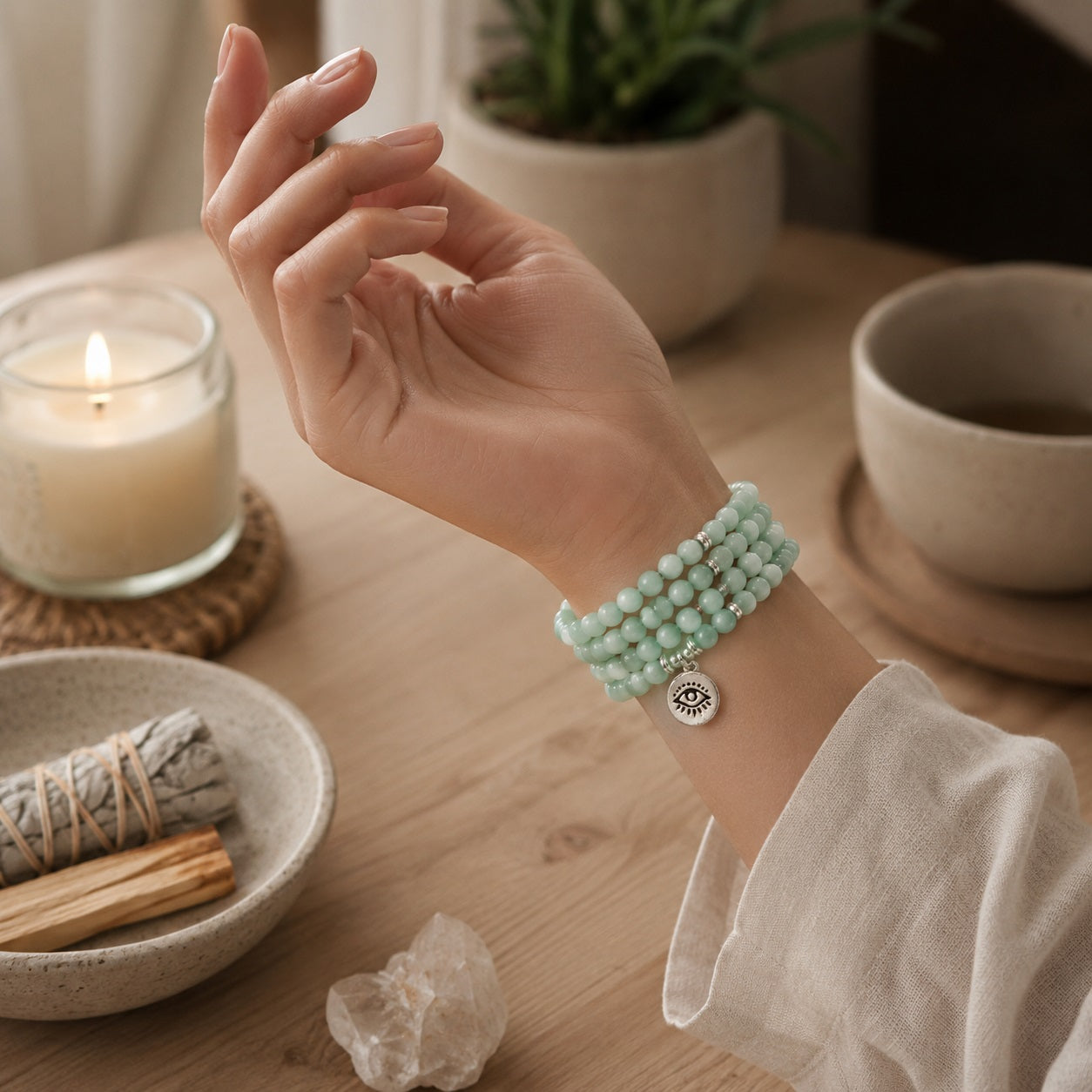 Woman wearing amazonite 108 bead mala as triple wrap bracelet with eye of truth pendant beside white sage smudge stick and candle crystal healing anxiety relief