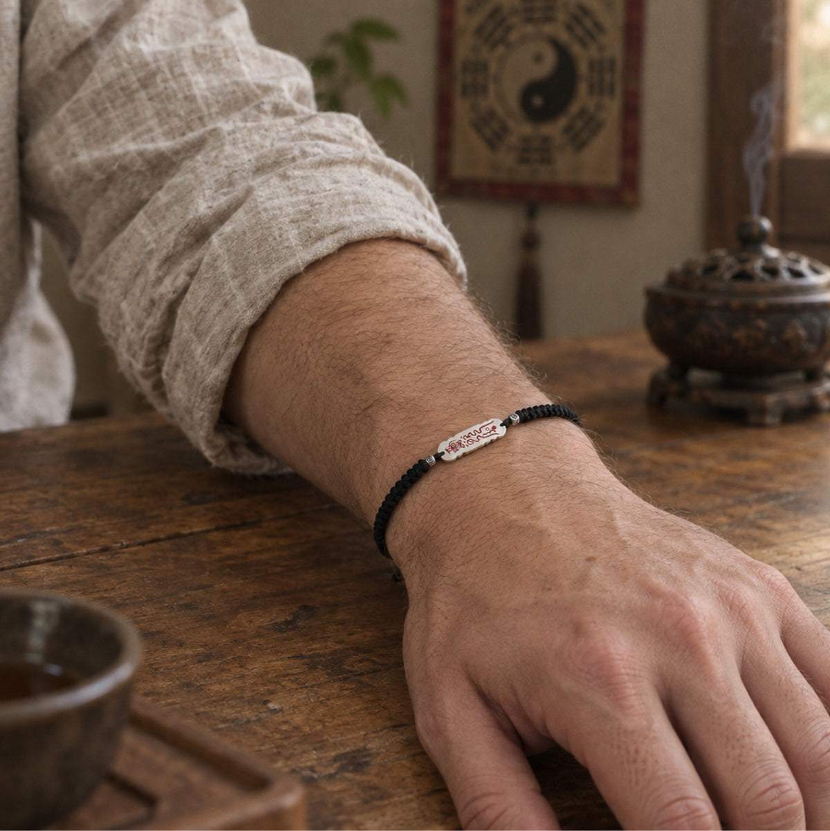 Man wearing the adjustable Taoist luck talisman bracelet, wrist resting on a wooden table