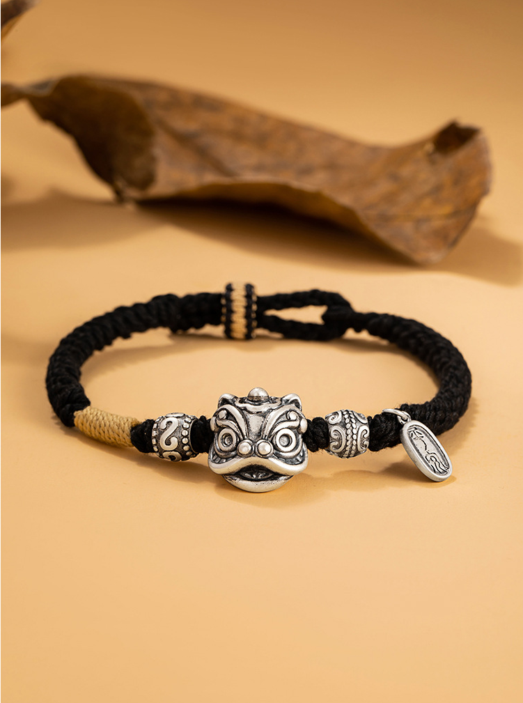 Men love protection bracelet with black braided cord silver lion head charm and rune beads closeup on warm yellow background with dried leaf Taoist KaiGuang guardian jewelry
