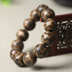 Men's luxury tiger stripe agarwood bracelet 18mm beads on redwood carved prop showing deep brown gold tiger stripe texture Taoist KaiGuang wealth meditation spiritual bracelet