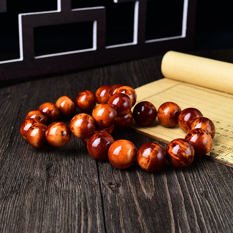 Men's stress relief cliff cypress bracelet 18mm beads laid on dark wood with bamboo scroll prop showing natural orange red grain texture Taoist KaiGuang grounding energy