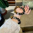 Two obsidian tiger eye protection strength bracelets different sizes woman hand display indoor natural light green plant background silver engraved spacer KaiGuang
