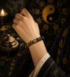 Woman wearing obsidian tiger eye protection strength bracelet silver engraved spacer bead wrist Taoist yin yang Tianshi temple dark background KaiGuang