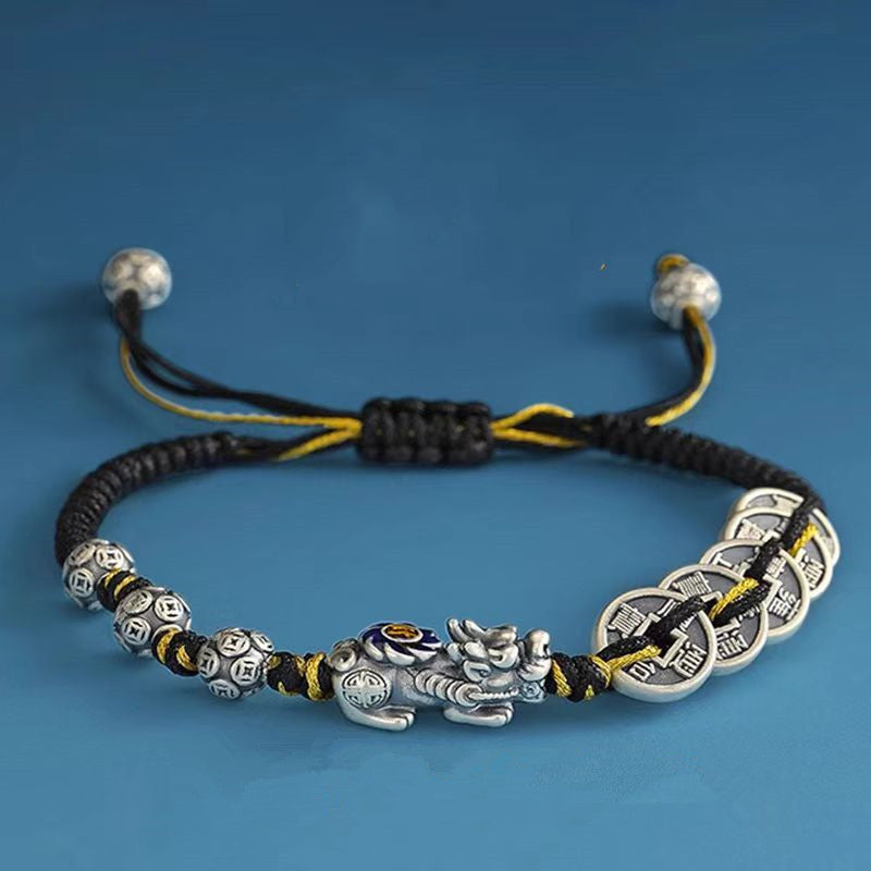 Pixiu wealth retention bracelet with black and yellow braided cord five ancient coin charms on clean blue background showing adjustable design