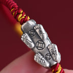 Close up of Pi Xiu charm underside showing engraved ancient coins and Taoist characters on red cord bracelet