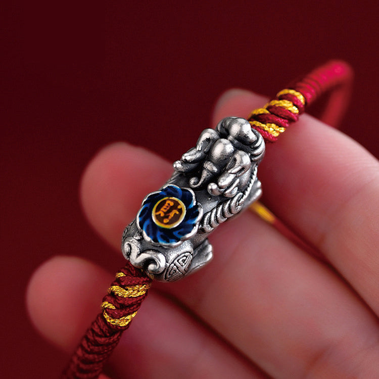 Hand holding red cord Pi Xiu bracelet close up showing silver beast with blue enamel lotus detail