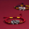 Red cord Pi Xiu KaiGuang bracelet on red background with silver wealth guardian charm centered