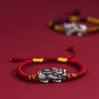 Red cord Pi Xiu KaiGuang bracelet on red background with silver wealth guardian charm centered