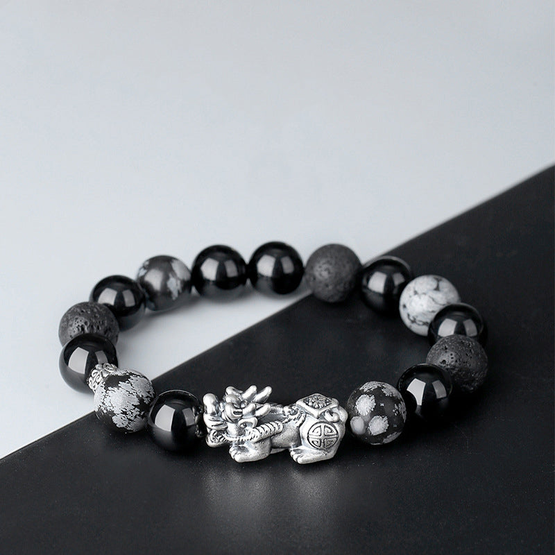 Pixiu obsidian KaiGuang fortune bracelet on black and white diagonal background showing silver Pixiu charm and bead contrast