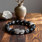  Pixiu obsidian volcanic stone Taoist KaiGuang wealth bracelet flat lay on dark wood surface with ceramic vase zen background