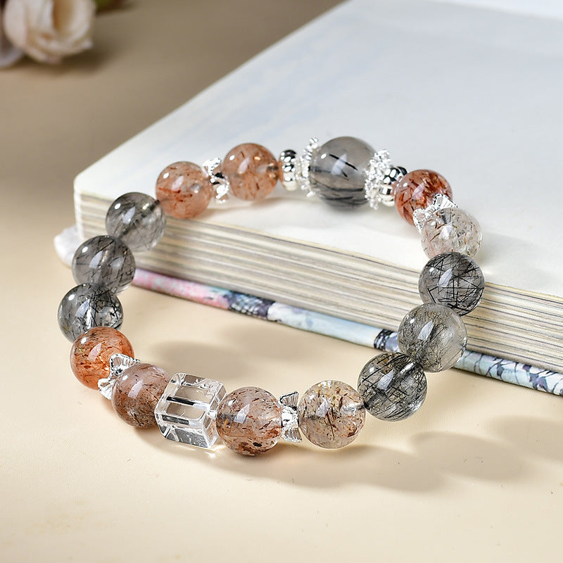 Black rutilated quartz strawberry quartz protection grounding bracelet silver crown spacers clear quartz cube bead leaning on book cream background KaiGuang