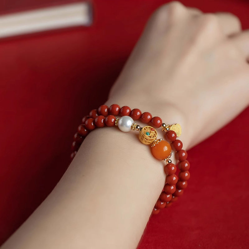 Red cinnabar bracelet worn on wrist against red background highlighting beeswax and pearl accent beads