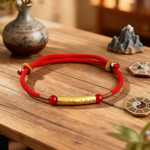 Red rope KaiGuang amulet bracelet with gold mantra tube and agate beads on wooden table beside Taoist decor