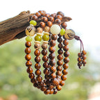 Rosewood 108 bead meditation mala four wrap bracelet with bodhi seed green jade and white jade accents hanging on driftwood natural green background Taoist KaiGuang grounding bracelet mindfulness