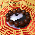 A close-up side view of a single 2.0cm aged thunderstruck wood bead with gold-painted Ten Character scripture, resting on a dark display stand for disaster relief.
