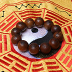 A close-up side view of a single 2.0cm aged thunderstruck wood bead with gold-painted Ten Character scripture, resting on a dark display stand for disaster relief.