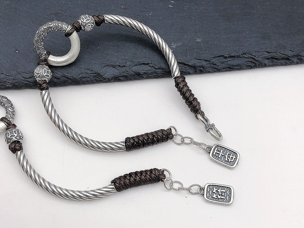 Two silver twisted rope peace buckle protection bracelets overlapping on slate and white surface white jade peace buckle ring carved silver cloud pattern beads ping an Chinese character charm pendant Taoist KaiGuang evil warding protection amulet