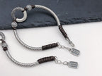 Two silver twisted rope peace buckle protection bracelets overlapping on slate and white surface white jade peace buckle ring carved silver cloud pattern beads ping an Chinese character charm pendant Taoist KaiGuang evil warding protection amulet