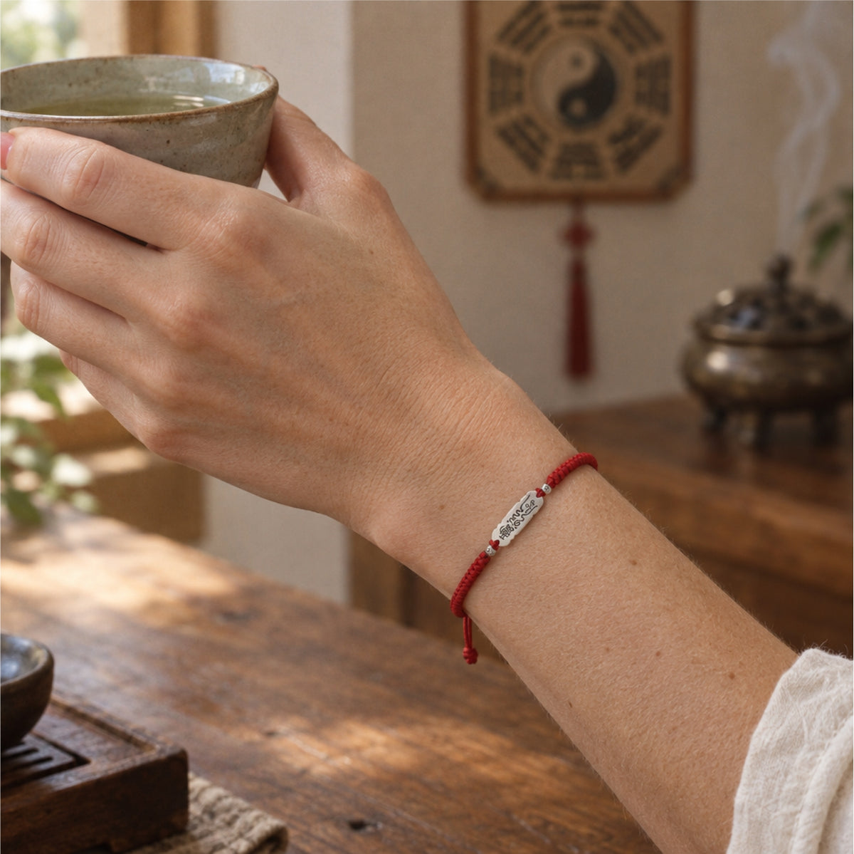 Woman holding a cup of tea while wearing the silver talisman red string bracelet