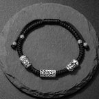 Taiji aura wealth guardian bracelet black braided cord sterling silver Pixiu and lock overhead view on dark stone Taoist KaiGuang blessing