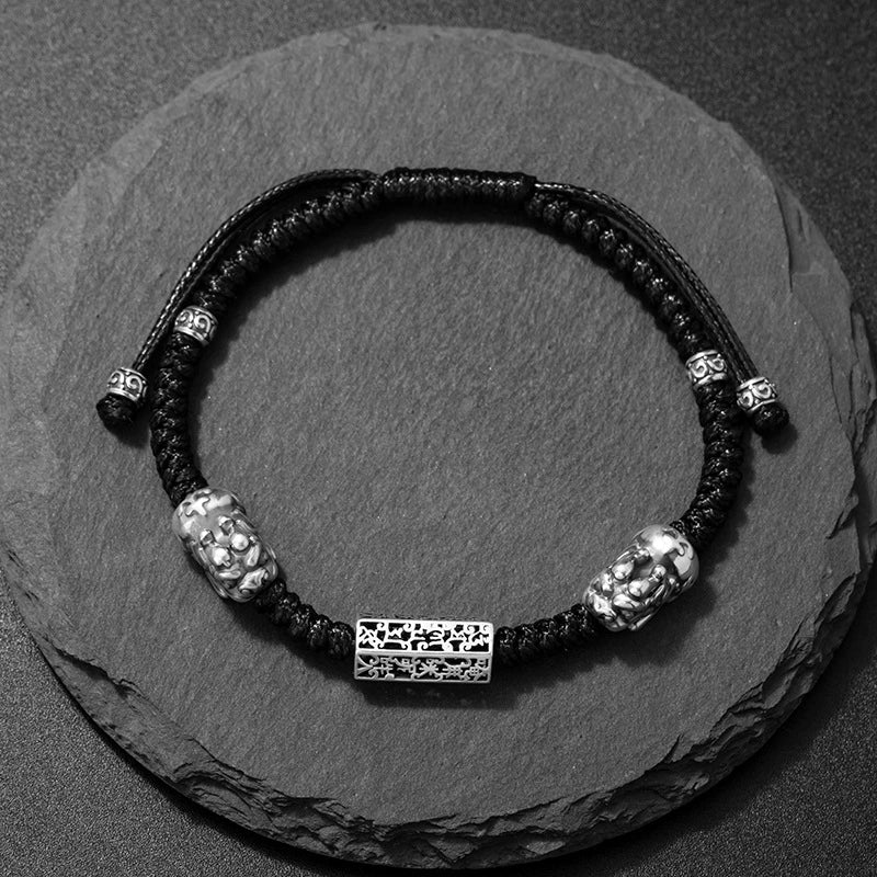 Taiji aura wealth guardian bracelet black braided cord sterling silver Pixiu and lock overhead view on dark stone Taoist KaiGuang blessing