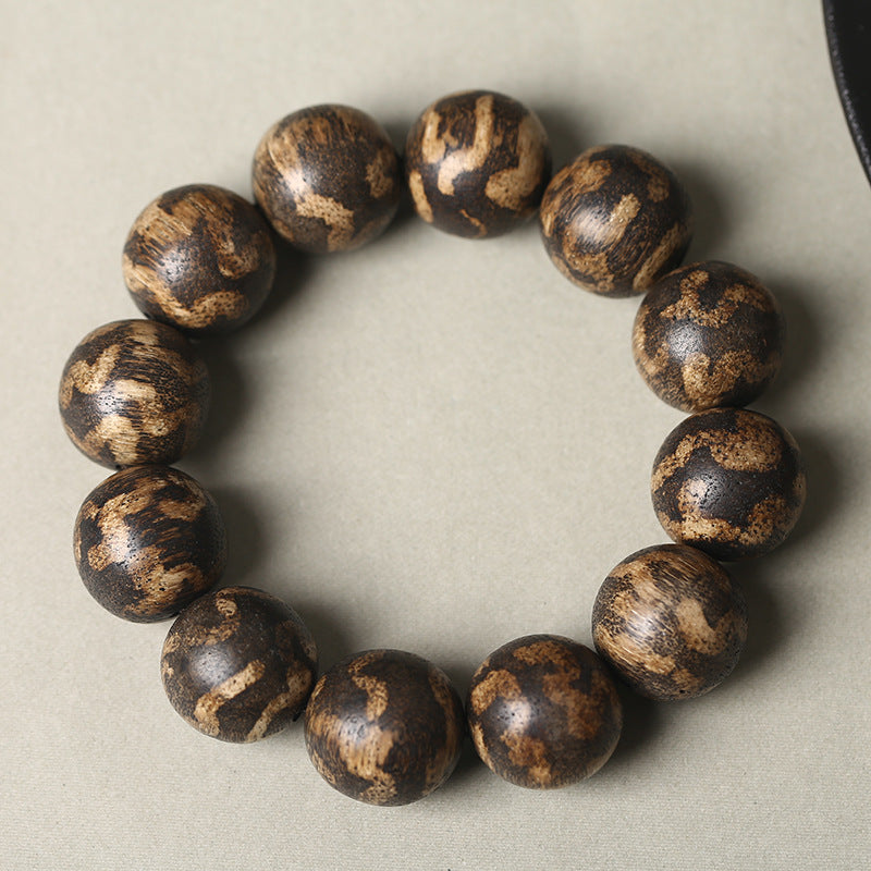 Full view of the 18mm Agarwood bracelet atop a traditional yellow scripture page, symbolizing the connection between ancient wisdom and personal protection.