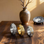 Three gold and silver Taoist KaiGuang spinner rings displayed on wooden table with vase