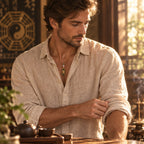 Man wearing a small black Taoist talisman pendant while adjusting his sleeve in a sunlit tea room.