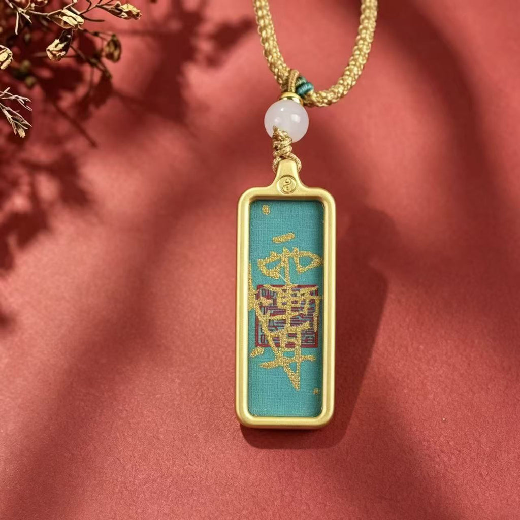 Front view of a teal Taoist talisman pendant with gold-colored markings and frame on a red background.