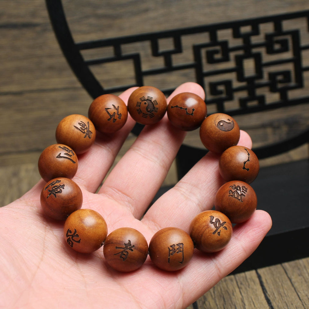 Hand holding thunderstruck jujube wood protection bracelet showing hand-engraved nine character mantra Lin Bing Dou Zhe Jie yin yang bagua symbols on large round beads dark Taoist lattice background spiritual protection