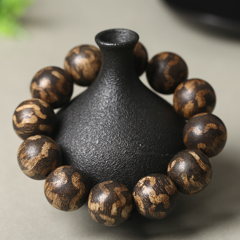 A high-oil natural Agarwood bracelet with distinctive tiger-stripe patterns, showcased on a traditional black ceramic vessel to represent spiritual harmony.