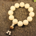  White bodhi root Taoist KaiGuang bracelet side view on linen showing polished bead surface and tassel