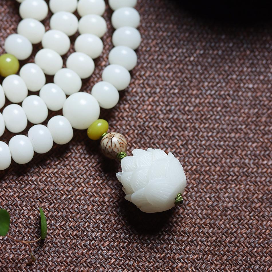 Intricately carved white jade sacred lotus pendant with bodhi seed spacer and emerald green accent bead on natural linen fabric background inner peace meditation clearing mental blocks
