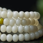 Close-up of high-density white jade bodhi root beads stacked in multiple rows showing smooth alabaster texture with single emerald yellow accent bead black background cognitive clarity mental detox tool