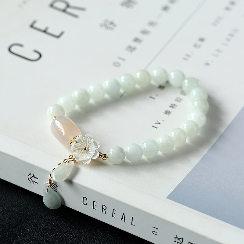 White jade fortune shift bracelet with floral charm displayed on white magazine against black surface minimalist style