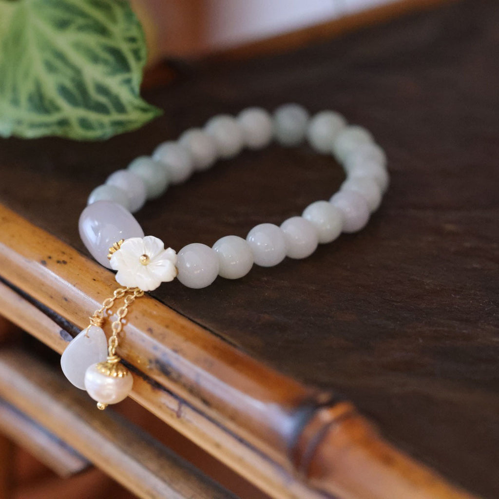 White jade KaiGuang aura cleanse bracelet resting on bamboo rail with tropical green leaf on dark wood table