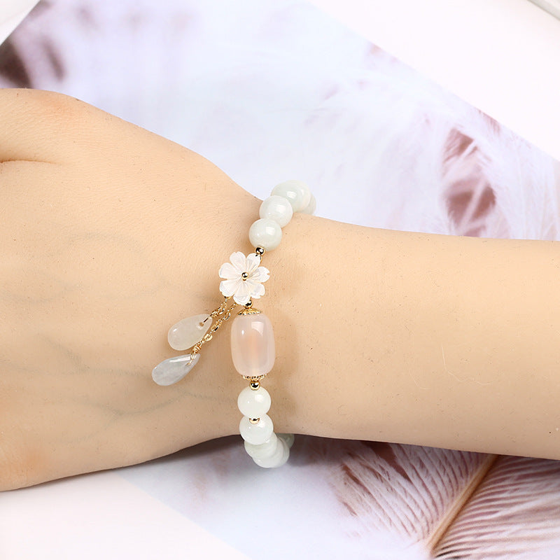 White jade Taoist KaiGuang emotional healing bracelet worn on female wrist with flower and jade drop charm on soft pink feather background