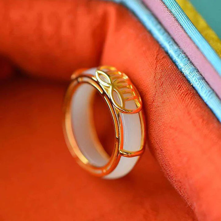 White jade KaiGuang luck fortune ring standing upright on orange background showing gold rim and band thickness