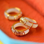White jade Taoist KaiGuang ring with gold trim lying on orange fabric showing natural white surface and gold pattern