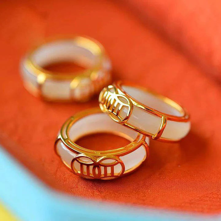 White jade Taoist KaiGuang ring with gold trim lying on orange fabric showing natural white surface and gold pattern