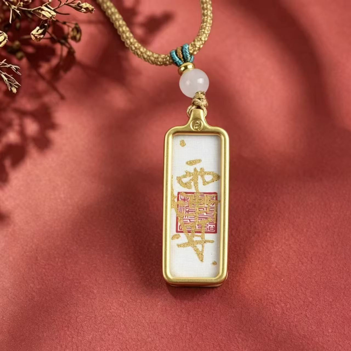 Front view of a white Taoist talisman pendant with gold-colored markings, a red square motif and a pale round bead.