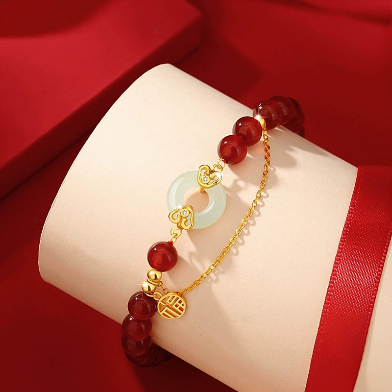 Women love attraction bracelet on white display stand showing red agate beads white jade peace clasp gold auspicious cloud connectors and Fu charm against red silk background
