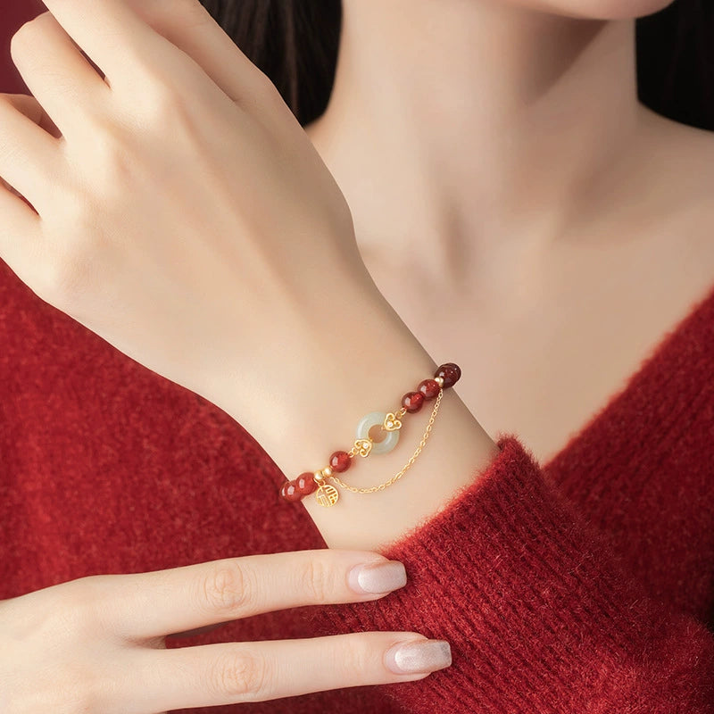 Woman wearing red agate love attraction bracelet with white jade peace clasp and gold Fu charm on wrist against red sweater background Taoist KaiGuang relationship protection jewelry