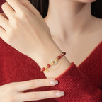 Woman wearing red agate love attraction bracelet with white jade peace clasp and gold Fu charm on wrist against red sweater background Taoist KaiGuang relationship protection jewelry